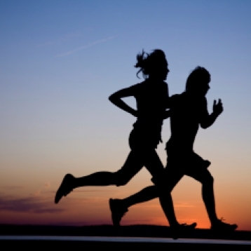 Young couple: man and woman run together on a sunset on lake coast. Silhouette.